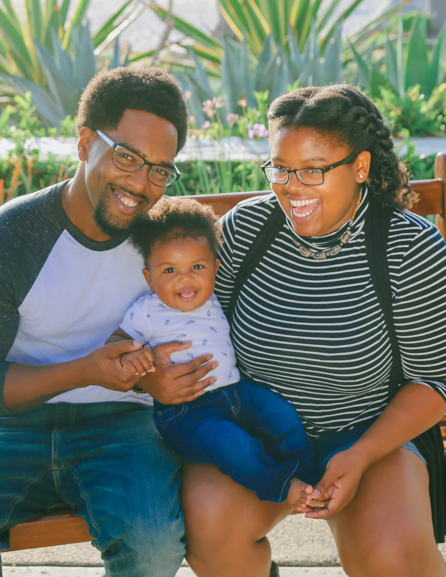 Two parents sitting outdoors with their baby, all three smiling