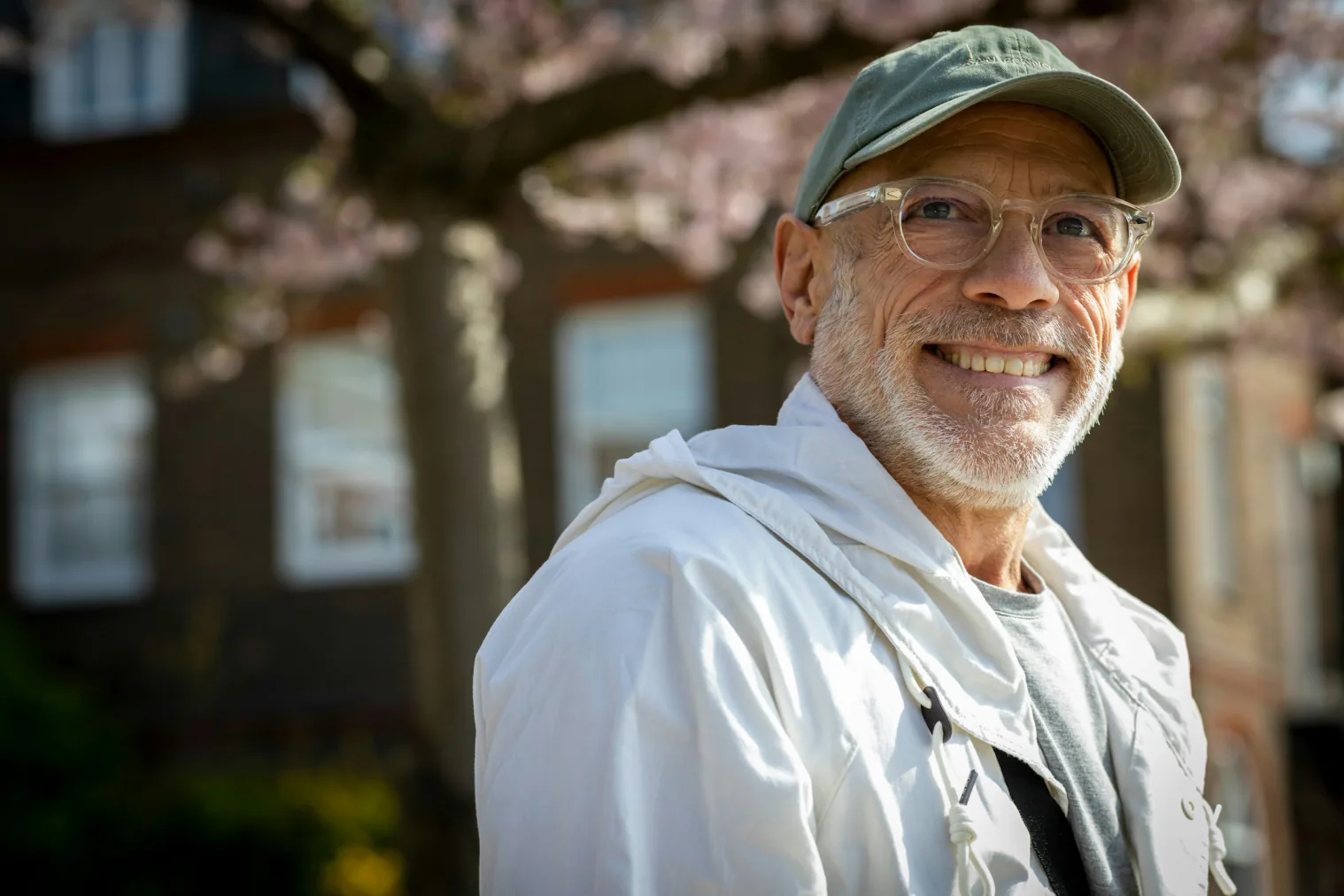 An older man in a ball cap smiling, outdoors on a spring day